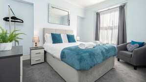 Quarto moderno com cama, mesa de cabeceira, abajur e uma cadeira.