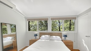A bedroom with a large bed, two bedside tables, a mirror, and three windows with a view of trees. - Riverside 3-bed Townhouse With Spacious Deck & BBQ (Mossy Point)