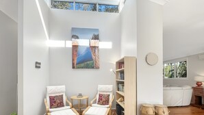 A modern living room with wooden flooring, two white armchairs with patterned cushions, a round coffee table, a bookshelf, and a large painting of a landscape. - Riverside 3-bed Townhouse With Spacious Deck & BBQ (Mossy Point)