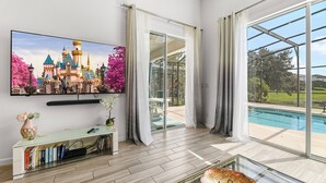 A spacious living room with a large flat-screen TV, a glass coffee table, and a bookshelf. - 4BR Retreat, Pool, Close to Disney (Kissimmee)