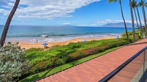 A beach view with palm trees, a wooden deck, and a clear sky. - Makena Surf B201 | 2nd Floor Oceanfront, On the Beach & Turtle Reef (Wailea)