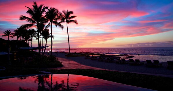 A beach resort with palm trees, lounge chairs, and a pool reflecting the sunset.