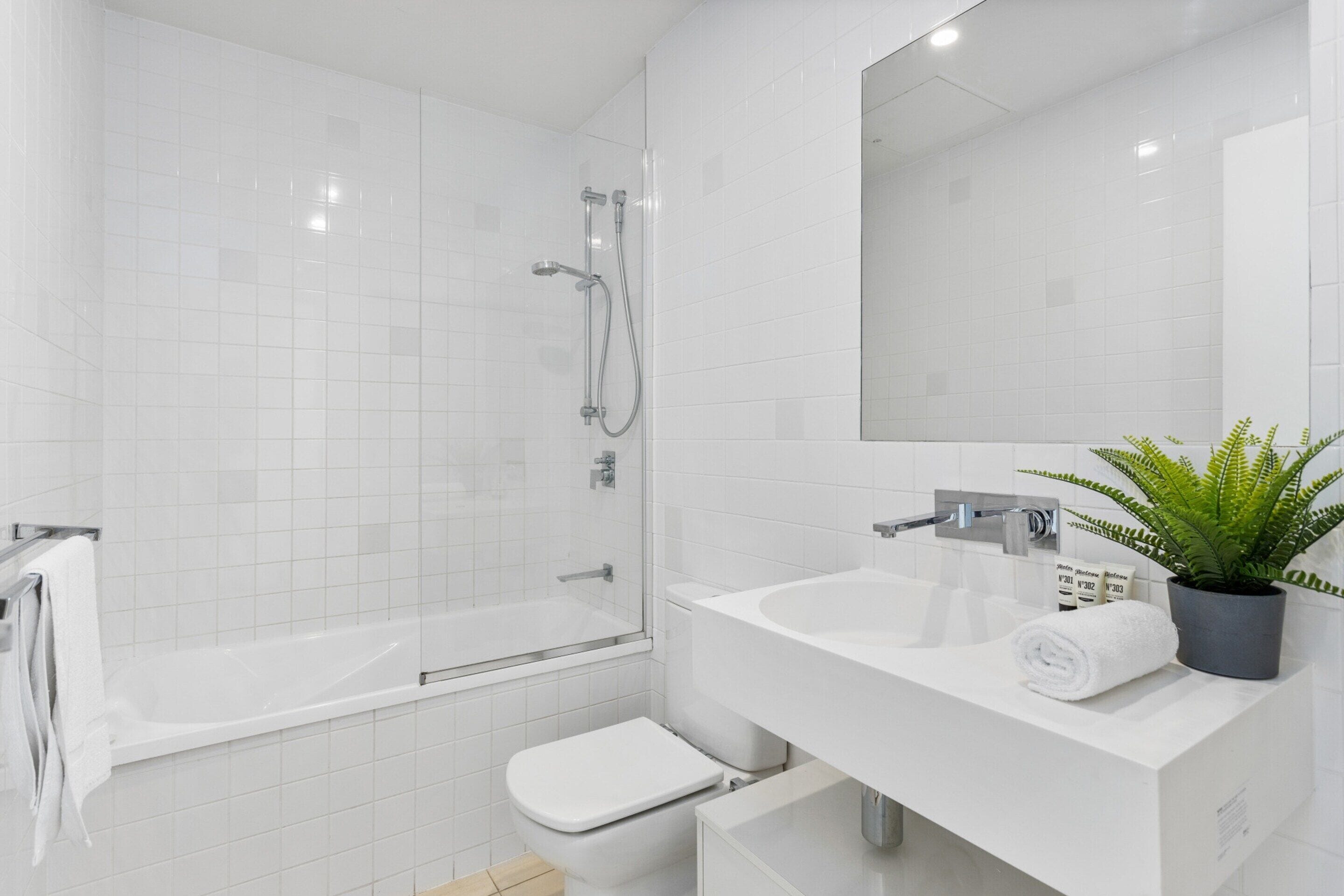 A modern bathroom with a glass-enclosed shower, a white toilet, and a sink with a mirror above it.