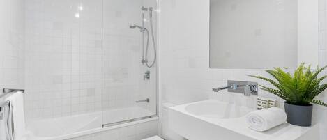 A modern bathroom with a glass-enclosed shower, a white toilet, and a sink with a mirror above it.