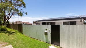 A fenced backyard with a grassy lawn, a wooden fence, and a house with a metal roof. - Relaxing 2-bed Home Close to Beaches and Parks (Sydney)
