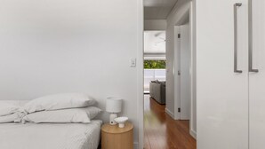 A modern bedroom with a bed, bedside table, and a view into the living area. - Relaxing 2-bed Home Close to Beaches and Parks (Sydney)