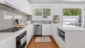 A modern kitchen with white cabinetry, a black stove, a dishwasher, and a window with blinds. - Relaxing 2-bed Home Close to Beaches and Parks (Sydney)