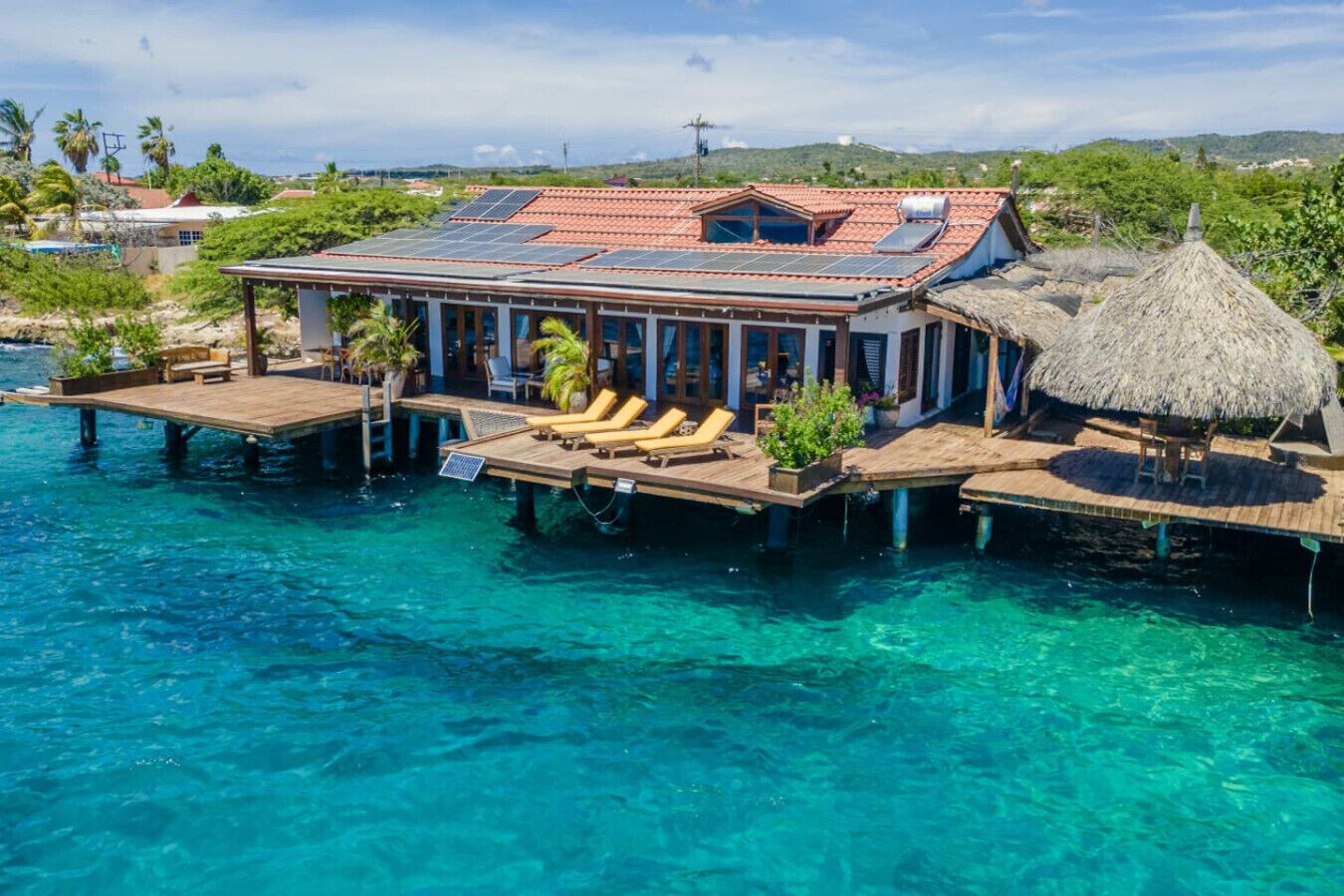 A beachfront property with a covered patio, lounge chairs, and a thatched-roof structure.