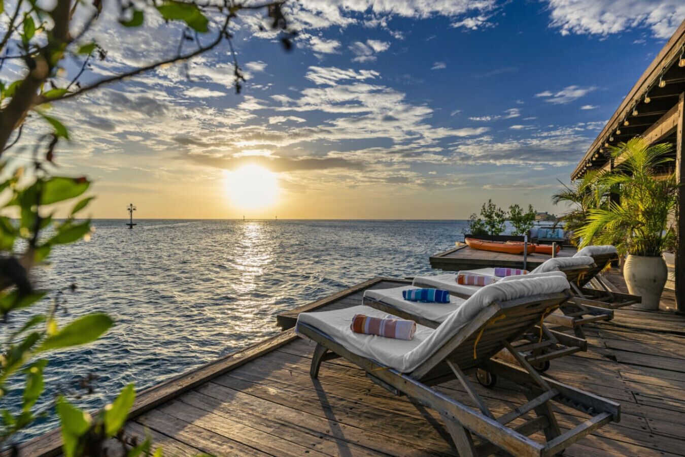 A wooden deck with lounge chairs and a view of the sea at sunset.