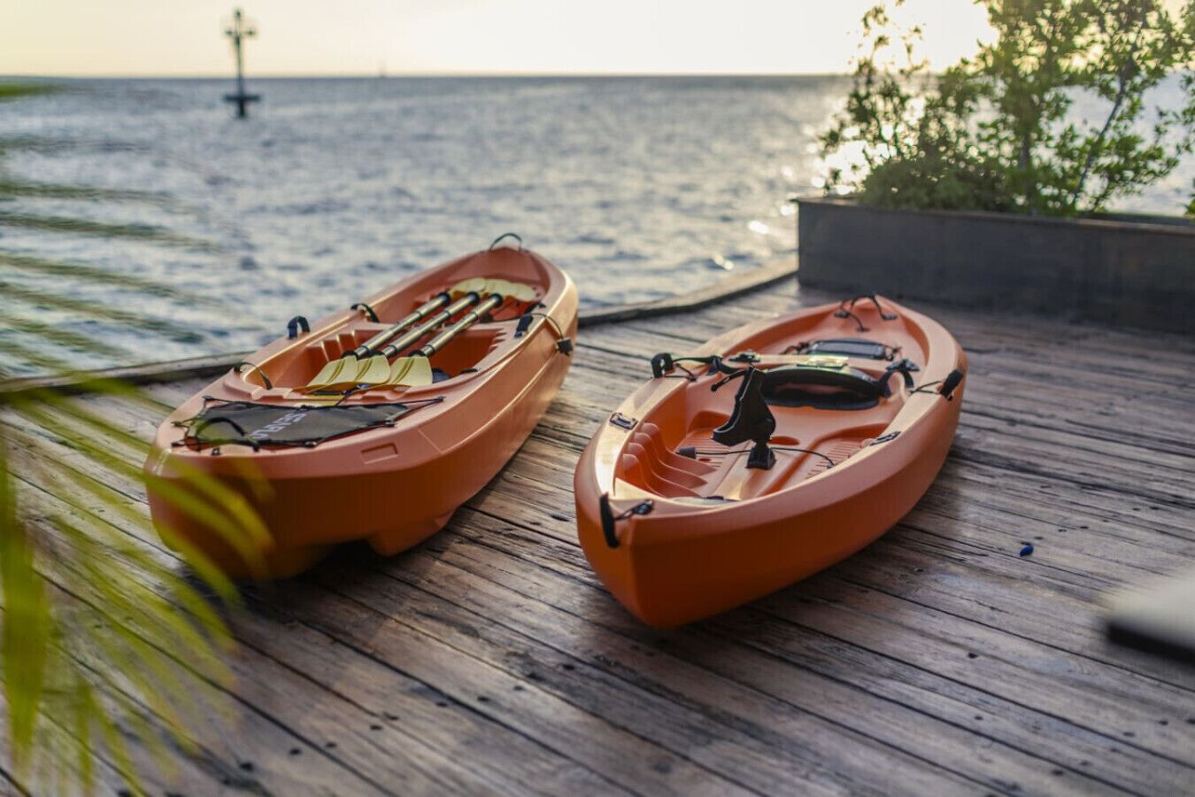 Two orange kayaks on a wooden dock by the sea.