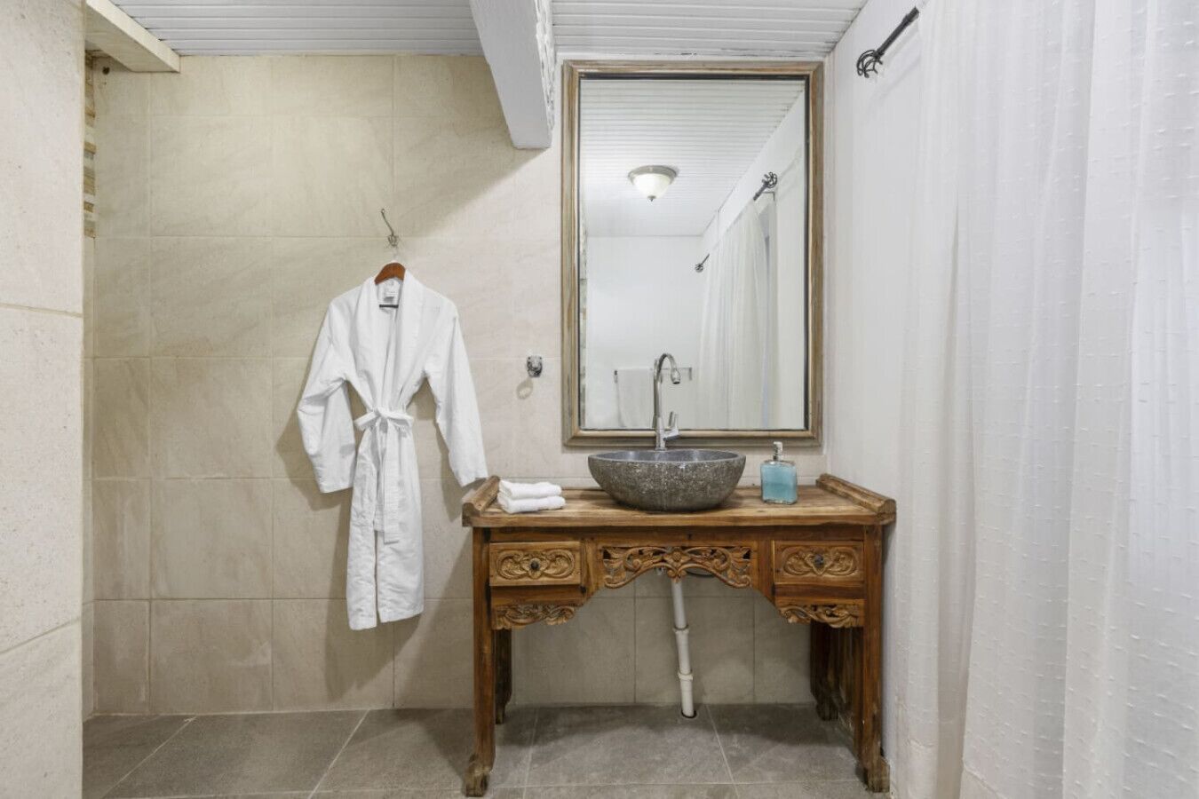 A bathroom with a white robe hanging on the wall, a wooden vanity with a stone sink, and a large mirror above the vanity.