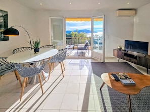 A modern living room with a dining area, a TV, and a balcony with a view.