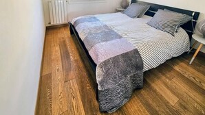 Ett sovrum med en säng, ett element, ett fönster och en tavla på väggen.