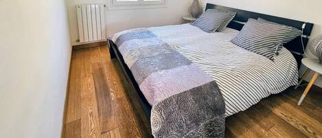 A bedroom with a bed, a radiator, a window, and a picture on the wall.