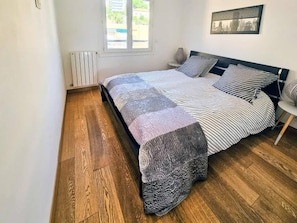 A bedroom with a bed, a radiator, a window, and a picture on the wall.