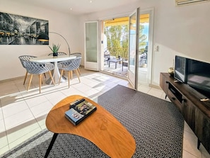 A modern living room with a sofa, a coffee table, a TV, and a dining area with chairs and a table.