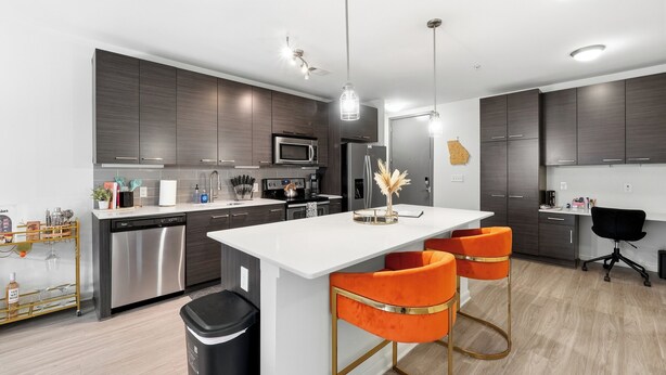Una cocina moderna con armarios de madera oscura, electrodomésticos de acero inoxidable y una isla blanca con taburetes naranja.