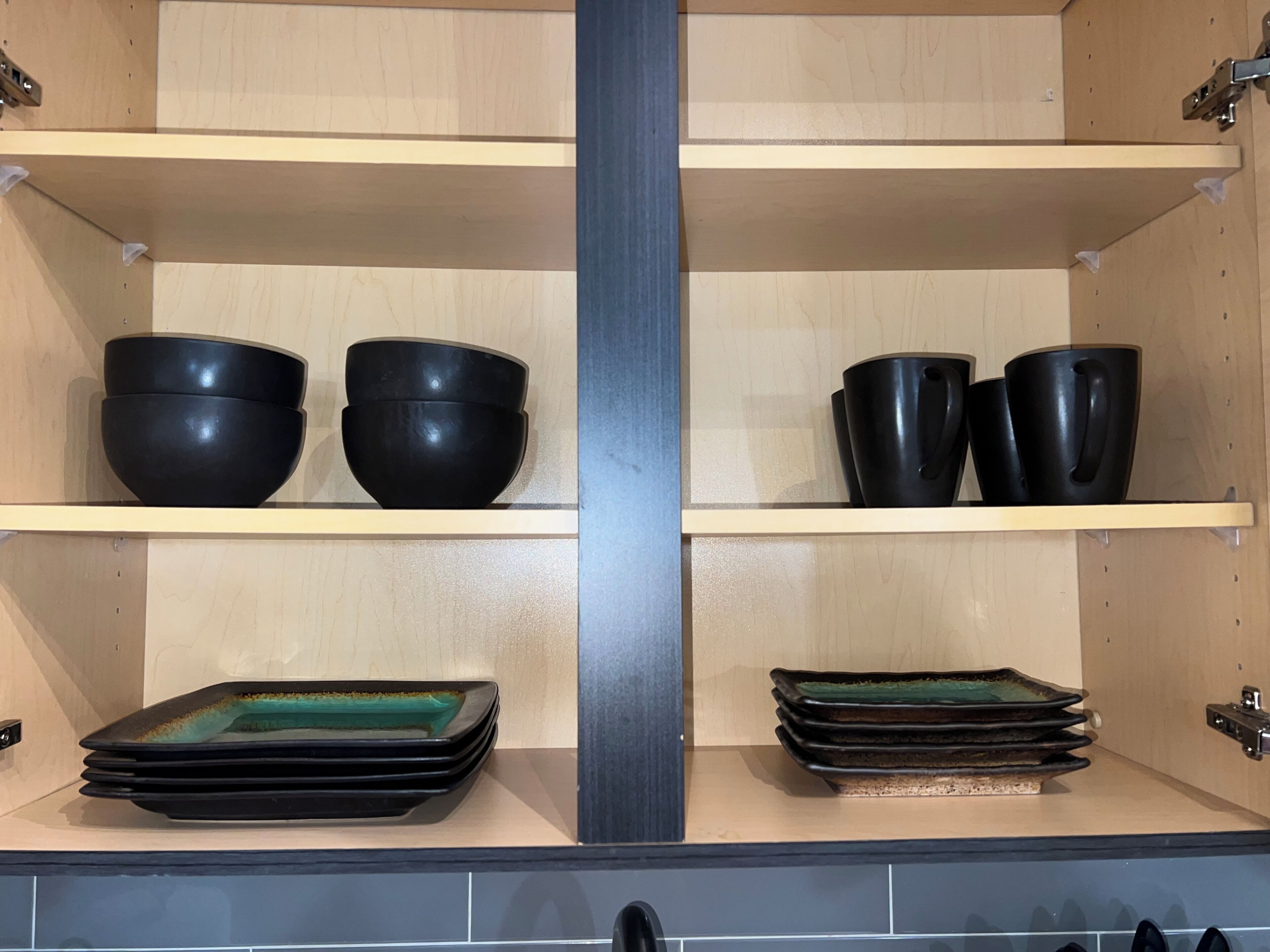 A kitchen with two shelves, each holding black bowls and plates.