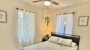 A bedroom with a bed, a nightstand with a lamp, and a window with curtains. - 3 BR Home Near Airport & Downtown (Austin)