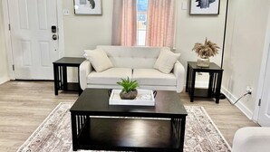 A living room with a sofa, a coffee table, two side tables, a floor lamp, and two framed pictures on the walls. - 3 BR Home Near Airport & Downtown (Austin)