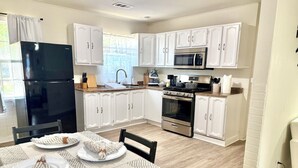 A modern kitchen with white cabinets, a black refrigerator, a microwave, and an oven. There is a dining table set with plates and napkins. - 3 BR Home Near Airport & Downtown (Austin)