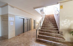 A hotel lobby with a marble staircase, elevators, and a sign indicating a connection to a nearby building.