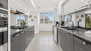 A modern kitchen with stainless steel appliances, a central island, and a view of the outdoors. - Scenic Beachside 3-bedroom With Water Views (Melbourne)