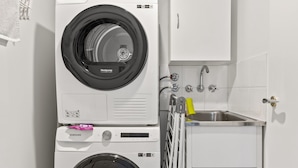A compact laundry area with two stacked washing machines, a small sink, and a cabinet. - Scenic Beachside 3-bedroom With Water Views (Melbourne)