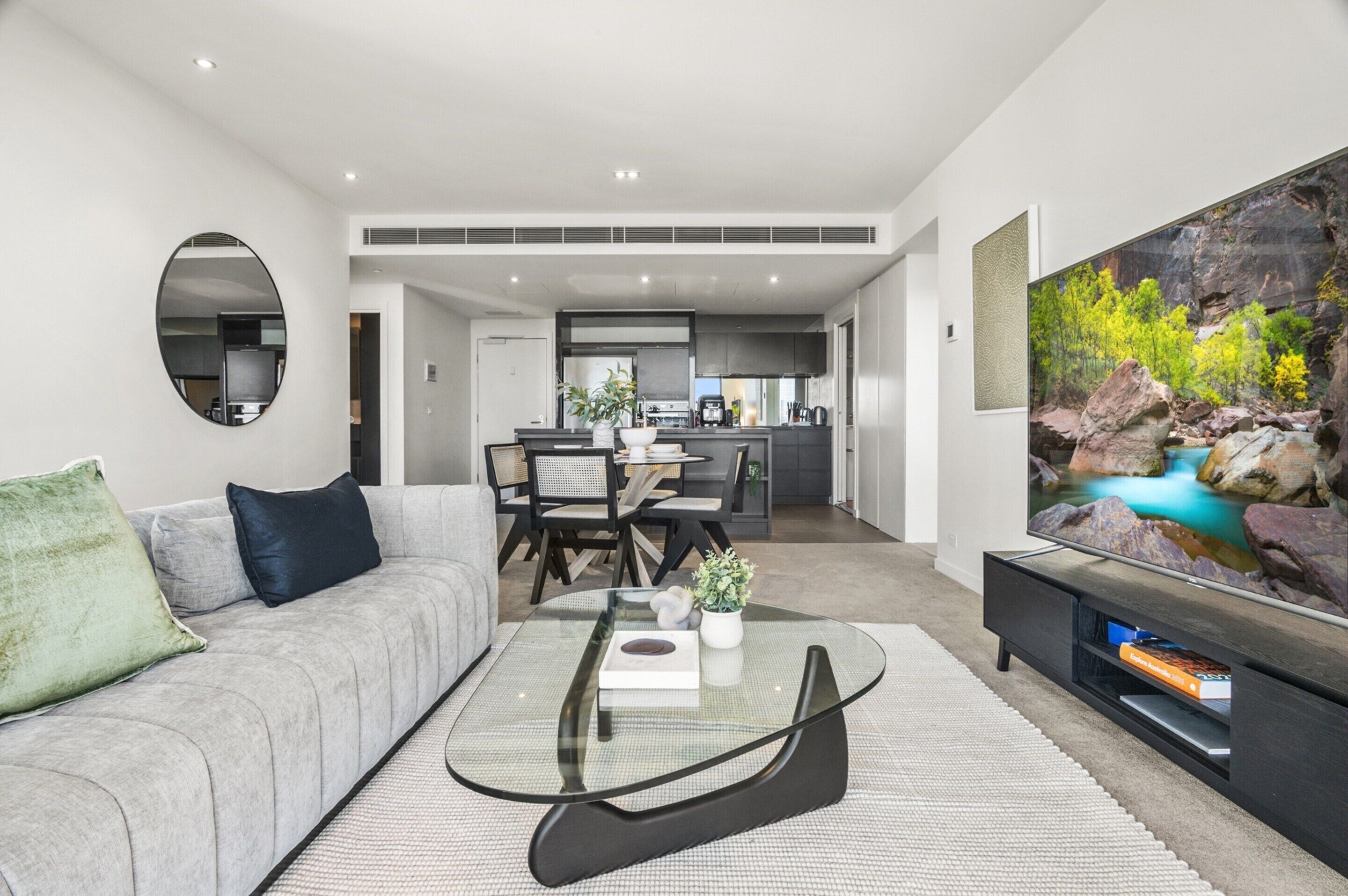 Ein modernes Wohnzimmer mit einem grauen Sofa, einem Glastisch und einem großen Flachbildfernseher.