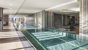 Uma piscina interior moderna com água cristalina, rodeada por paredes de vidro e chão em mosaico.