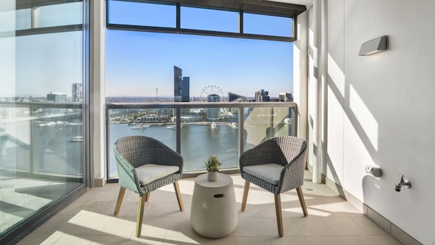 Uma varanda com duas cadeiras de vime, uma mesinha com uma planta e vista para o horizonte urbano, incluindo uma roda gigante.