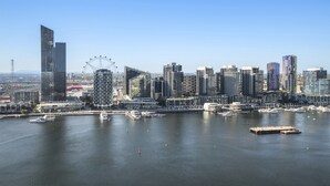 Paisagem urbana costeira com edifícios modernos altos, uma roda-gigante destacada e um porto com barcos.