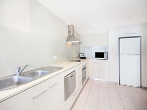 A modern kitchen with stainless steel appliances, a double sink, and white cabinetry. - Coastal 1-bed Escape Located in Twin Towns (Tweed Heads)