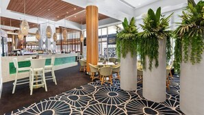 Un hall d’hôtel moderne, avec un tapis à motifs, une colonne centrale en bois et des plantes en pot.