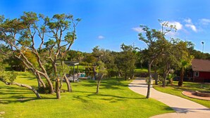 Um parque com um caminho pavimentado, árvores e um edifício vermelho ao fundo.
