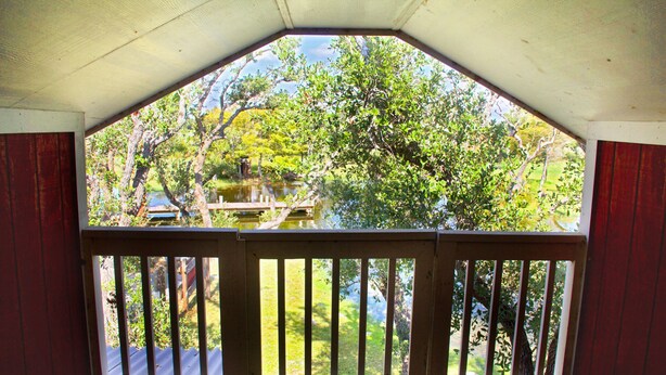 Um espaço ao ar livre coberto, com guarda de madeira, e vista para um jardim e uma casa.