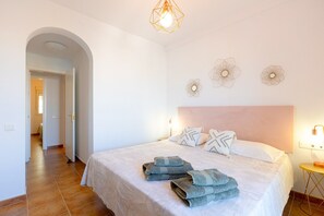 Ein Schlafzimmer mit einem Bett, Handtüchern, einem Kopfteil, Wandbildern und einer Tür zu einem anderen Raum.