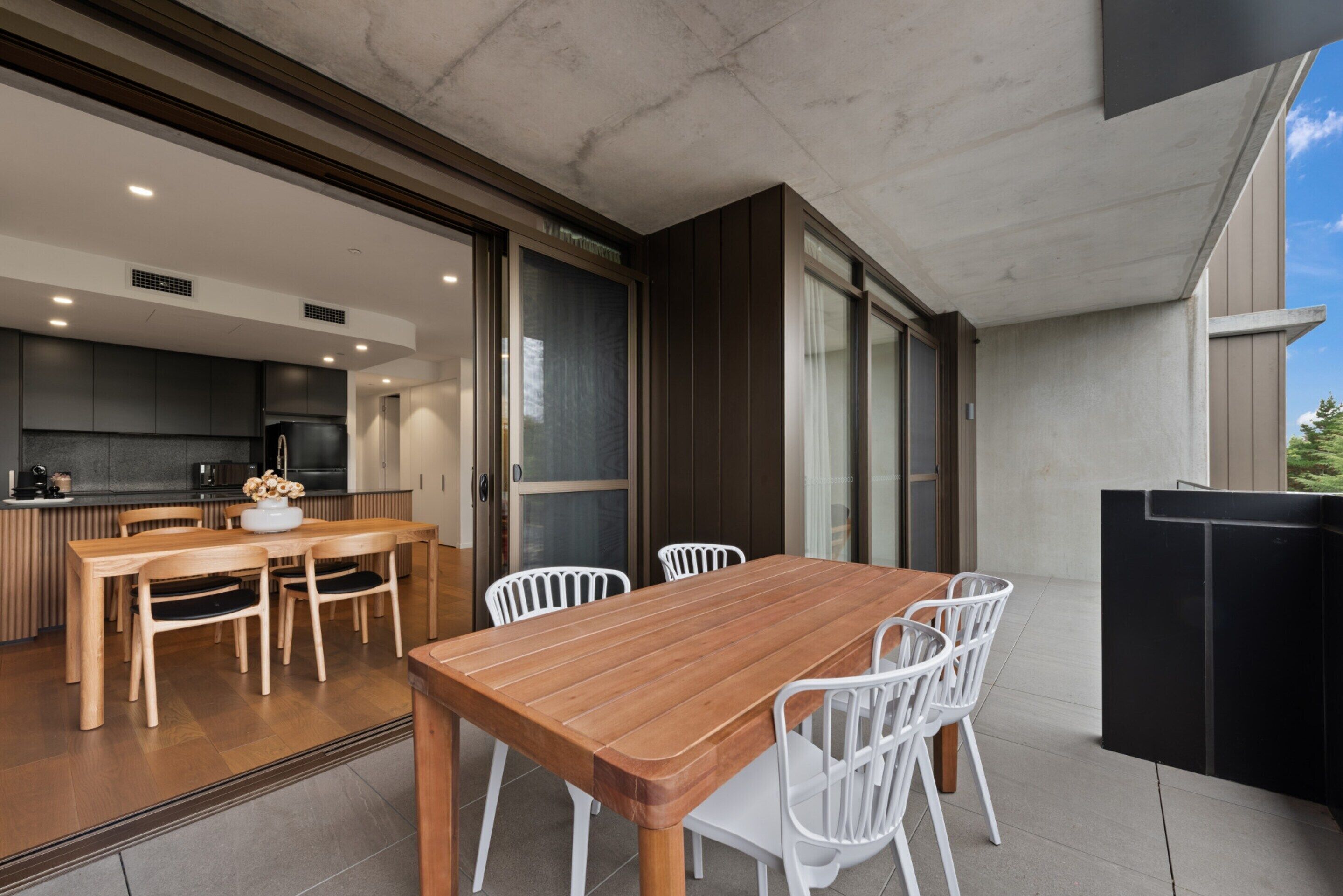 A modern kitchen with dark cabinets, a wooden dining table, and white chairs.