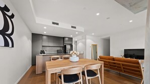 A modern living space with a wooden dining table, chairs, a sofa, and a kitchen area. - Stylish 2-bed in Braddon With Alfresco Dining (Canberra)