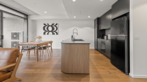A modern kitchen with a central island, wooden dining table, and chairs. - Stylish 2-bed in Braddon With Alfresco Dining (Canberra)