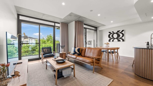 A modern living room with a leather sofa, wooden coffee table, and a dining area with a table and chairs. - Stylish 2-bed in Braddon With Alfresco Dining (Canberra)
