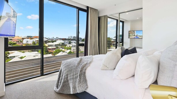 Quarto de hotel moderno com uma cama grande, televisão e vista para a cidade através de amplas janelas.