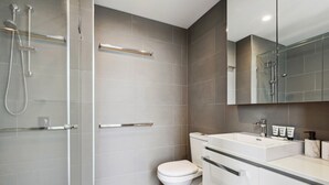 Uma casa de banho moderna com cabine de duche em vidro, sanita branca e espelho sobre lavatório.