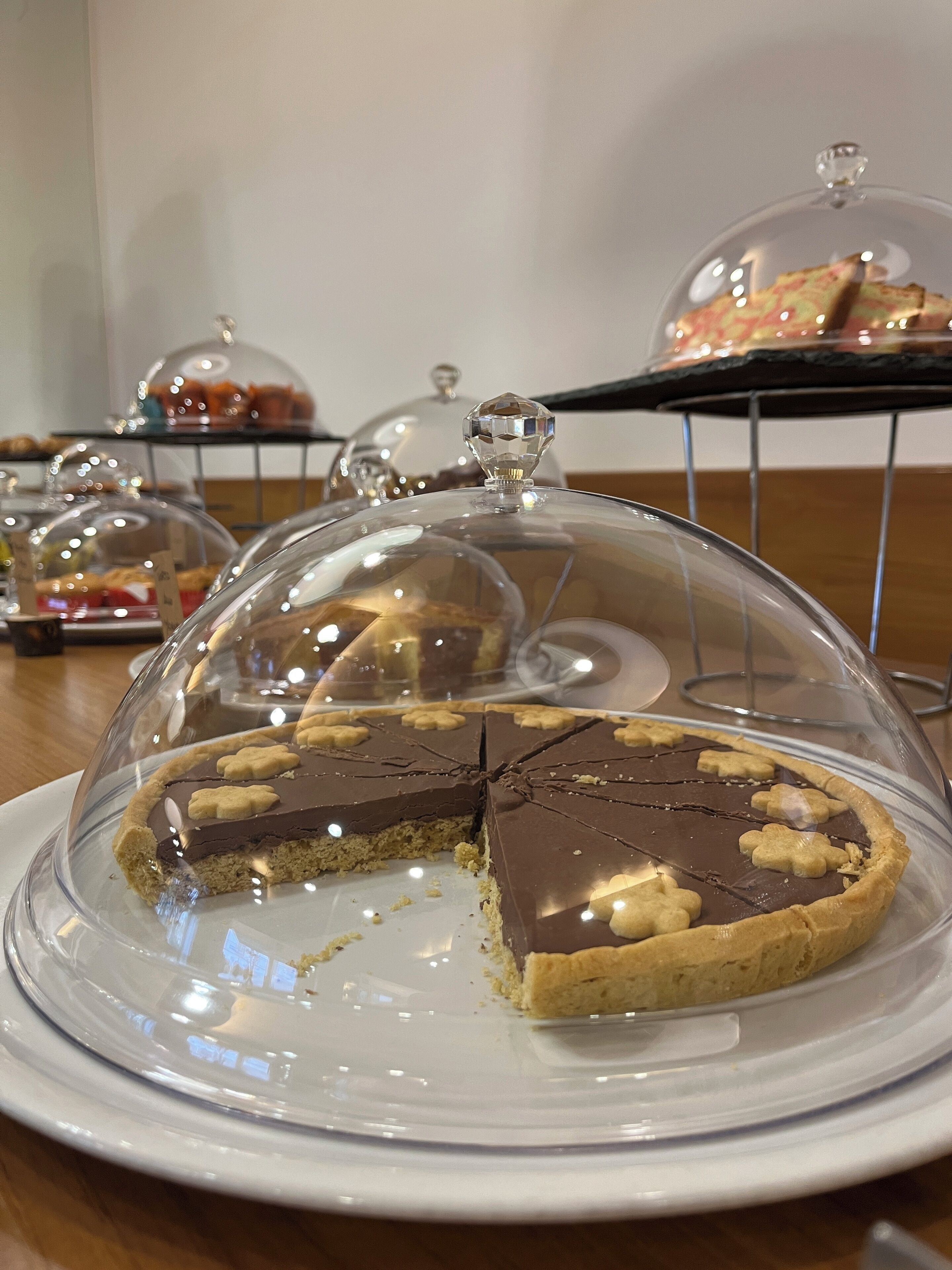 A dessert display with a pie under a glass dome, surrounded by other covered desserts.