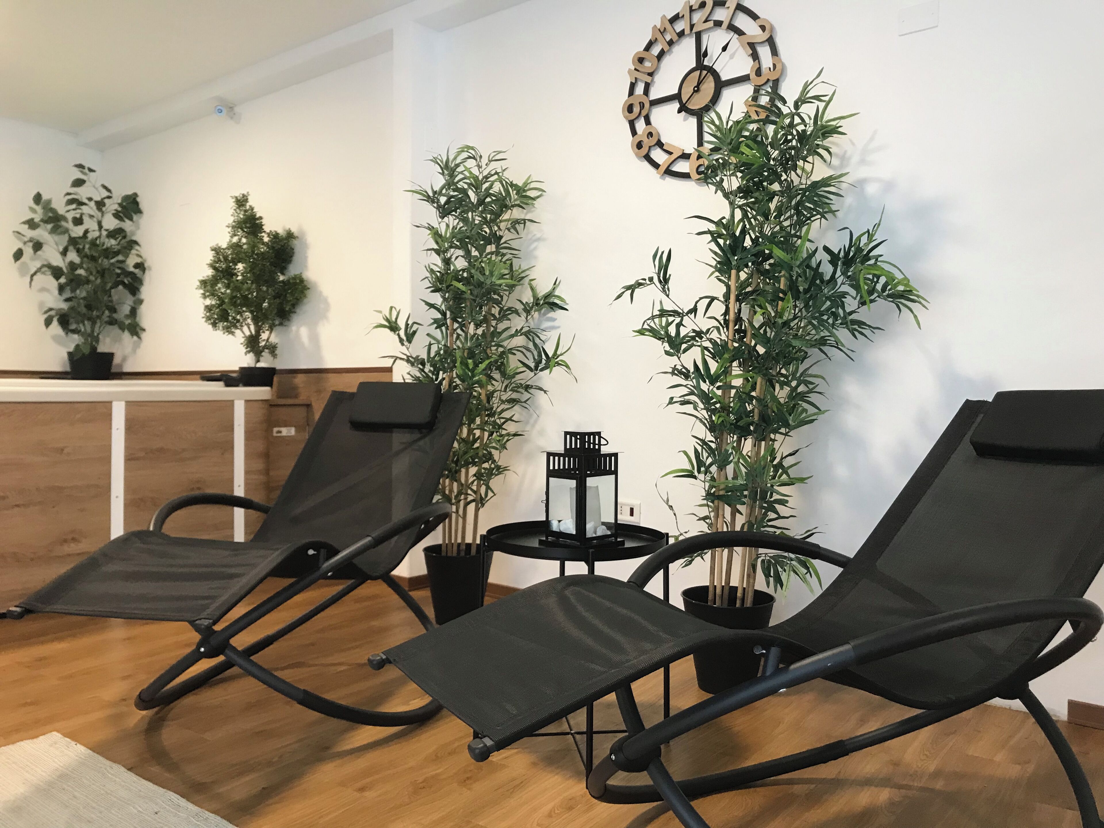 Une pièce comprenant deux fauteuils noirs, un comptoir d’accueil en bois et plusieurs plantes en pot.