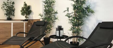 Une pièce comprenant deux fauteuils noirs, un comptoir d’accueil en bois et plusieurs plantes en pot.