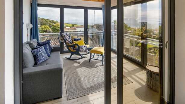 Ein modernes Wohnzimmer mit einer Couch, einem Schaukelstuhl und Blick auf die Landschaft durch große Fenster.