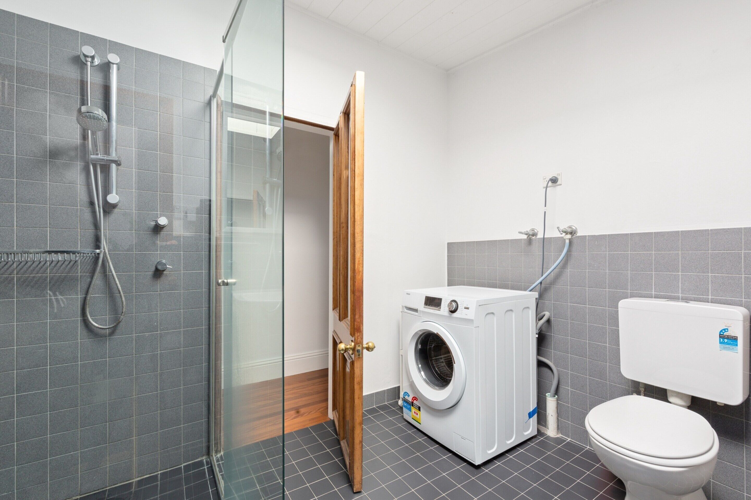 Un baño pequeño con cabina de ducha de vidrio, lavadora e inodoro.