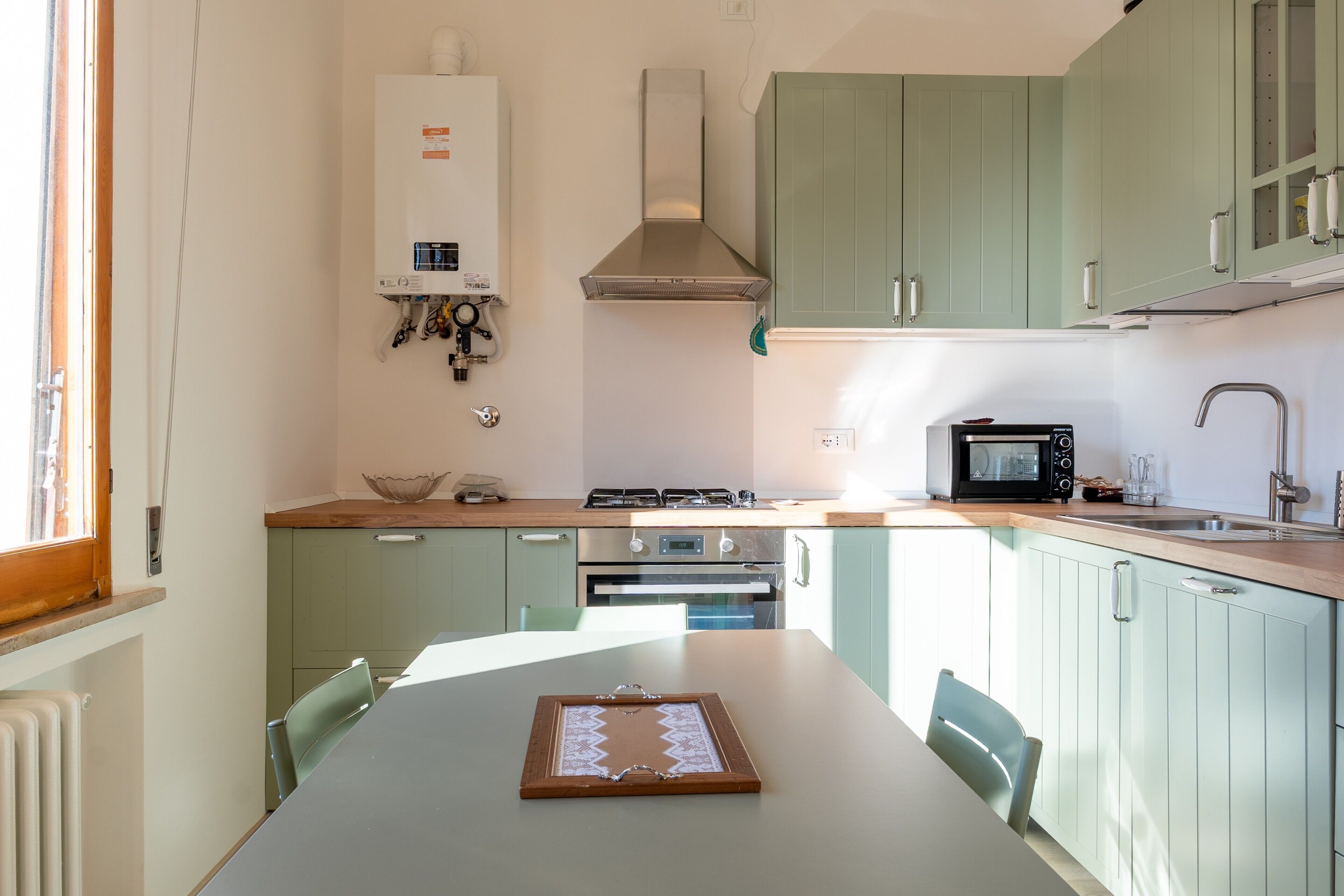 Una cocina con una mesa, sillas, microondas, horno y calentador de agua.