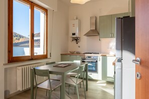 Keittiössä on ikkuna, patteri, pöytä ja tuolit, liesi sekä jääkaappi.